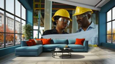 Diverse African male and female construction worker team examining blueprints industrial building Wall mural