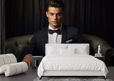 A young handsome man wearing a suit and a bow tie sitting in an armchair and looking at the camera Wall mural