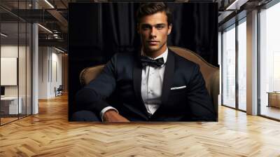 A young handsome man wearing a suit and a bow tie sitting in an armchair and looking at the camera Wall mural