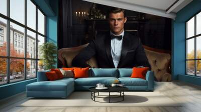 A young handsome man wearing a suit and a bow tie sitting in an armchair and looking at the camera Wall mural