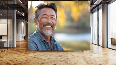 Asian american man in his 50s who exudes happiness and a sense of feeling truly alive in a beautiful natural park near lake, genuine smile on his face, relaxed and confident male who found joy Wall mural