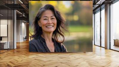 Asian american woman in her 50s who exudes happiness and a sense of feeling truly alive in a beautiful natural park near a lake, genuine smile on her face, relaxed and confident, female who found joy Wall mural