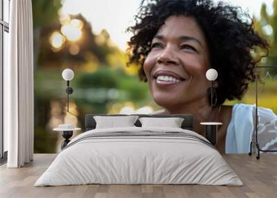 Black american woman in her 50s who exudes happiness and a sense of feeling truly alive in a beautiful natural park near a lake, genuine smile on her face, relaxed and confident, female who found joy Wall mural