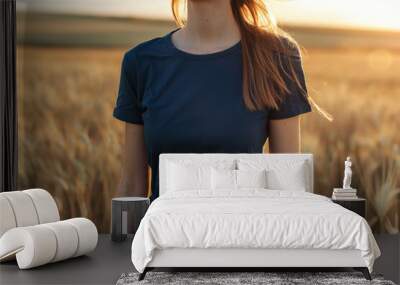 Caucasian female model wearing a navy blue crewneck blank mockup t-shirt with short sleeves in a field background at sunset , woman face is not visible Wall mural