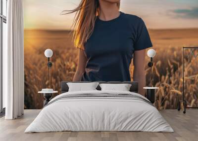 Caucasian female model wearing a navy blue crewneck blank mockup t-shirt with short sleeves in a field background at sunset , woman face is not visible Wall mural