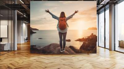 Confident woman with backpack with arms up relaxing at sunset seaside during a trip , traveler enjoying freedom in serene nature landscape Wall mural