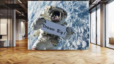 Dream big concept image with an astronaut in space holding a board sign with written words Dream Big Wall mural