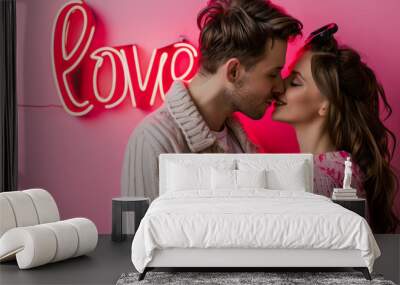 Love concept image with lovely man and woman couple kissing in front of a glowing love sign and pink background Wall mural