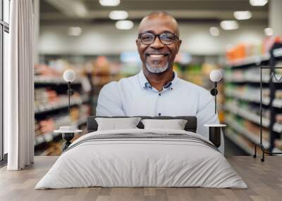 Portrait of a mature supermarket manager man with a kind smile inside his shop , grocery store shelves in background Wall mural