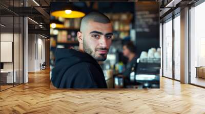 Portrait of young Persian man in a morning coffee shop wearing a black hoodie looking at the camera Wall mural