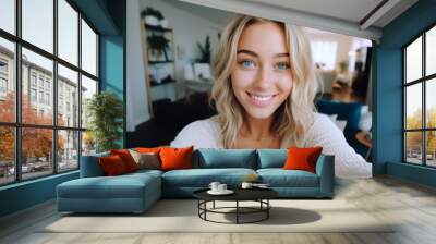 Selfie picture of a happy young pretty millennial woman smiling at the camera in the living room in a modern home Wall mural