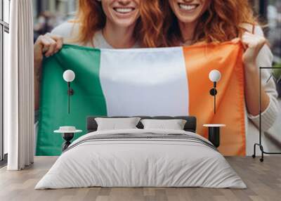 Two irish cheerful woman friends holding a Ireland flag on dublin city street Wall mural