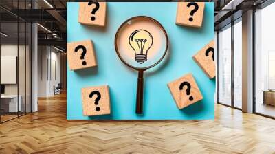 A glowing light bulb under a magnifying glass among cubes with question marks symbolizes thinking and ideas Wall mural