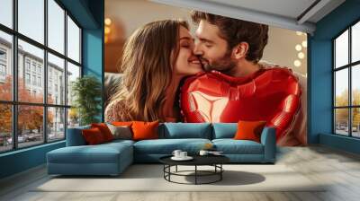 A young couple in love holds a heart-shaped balloon and covers themselves with it during a kiss Wall mural