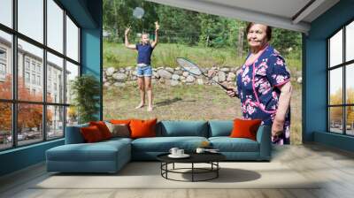 Aged grandma with her granddaughter playing badminton on backyard at summer season Wall mural