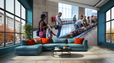 Family waiting their suitcase on baggage carousel in airport terminal Wall mural