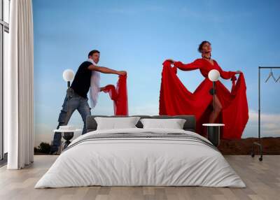 A model girl is preparing for a photo shoot on sand dunes and a male assistant helps her. A man helping a woman with posing with light cloth on nature landscape Wall mural