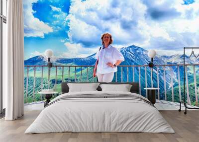 A woman on a balcony admires a stunning mountain range Wall mural