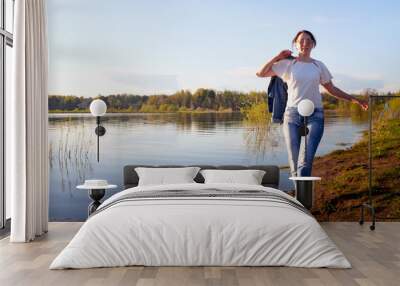 Girl or woman walking on the shore or beach of the lake in the evening at sunset. Wall mural