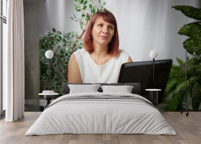 Serious girl with laptop and a notebook is working at a table in cozy room with flowers. A middle-aged business woman. Psychologist in the office Wall mural