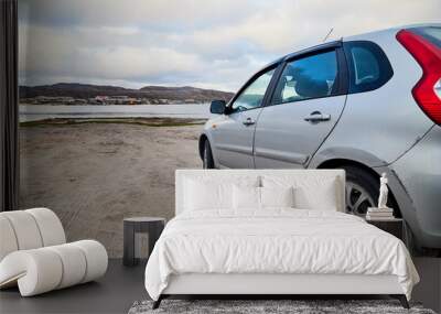 Small car standing on the side of road near wate of lake, river, fiord, sea and ocean. Wall mural