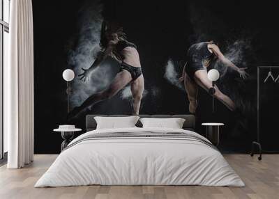 Two girls dance with flour in studio on black background, lights behind them and people helped girls Wall mural