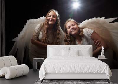 Two teenage girl in white dress and with white wings in a dark studio with bright flash. Sisters and models posing for a photo shoot like an angel Wall mural