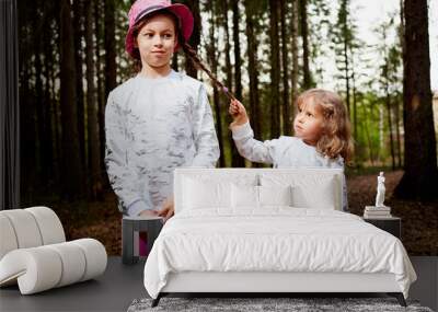 Two young girl playing and having fun together on walk in forest outdoors. Happy loving family with two sisters or female friends posing on nature landscape with with pine trees. Wall mural