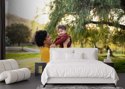 adorable toddler boy is lovingly held by adoring mother outside at sunset Wall mural