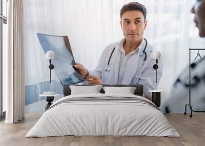 Male doctor in white medical uniform explaining x-ray results to female patient on consultation. They Consult Digital Tablet Computer while Talking about Patient's Health. Wall mural