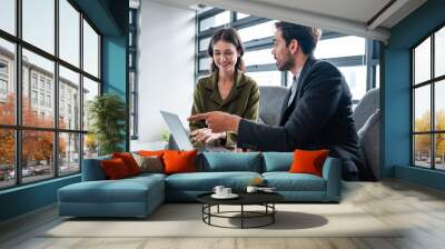 Two happy business woman and man using laptop working on computer at workplace. Cheerful young professional multiethnic colleagues team discussing online digital technology corporate project in office Wall mural