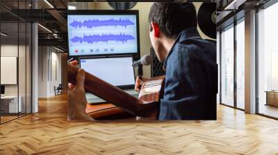 Young musician singing and playing guitar to record a song in his room. Music studio at home. Wall mural