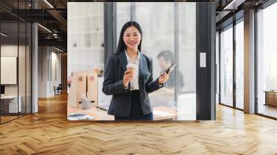 A confident woman in suit holds coffee and phone in modern office Wall mural