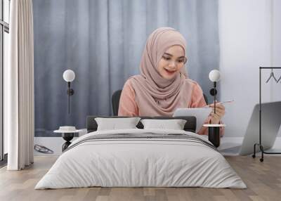 Beautiful asian muslim woman brown hijab having video call with friends or lover, using digital tablet at her home. Wall mural