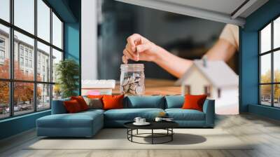 Close-up of a hand putting coins into a jar symbolizing saving money for real estate or financial investment purposes. Wall mural