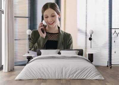 Happy professional millennial businesswoman in casual attire is making a business call while analyzing financial data on financial report at her office. Wall mural