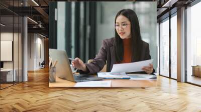 Happy smiling business woman working with laptop computer with paperwork at desk in a modern office, business finance technology concept. Wall mural