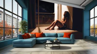 Sad and depressed young woman sitting on the floor in the living room looking outside the doors,sad mood,feel tired, lonely and unhappy concept. Selective focus Wall mural