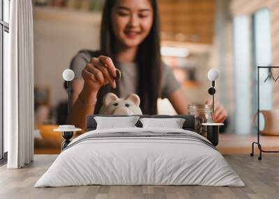 Saving money is important habit, as shown by young woman joyfully depositing coins into piggy bank while surrounded by jar of coins. This scene captures essence of financial responsibility and Wall mural