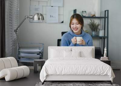 Smiling young woman enjoying a warm beverage during a break in a modern home office. Work life balance concept Wall mural