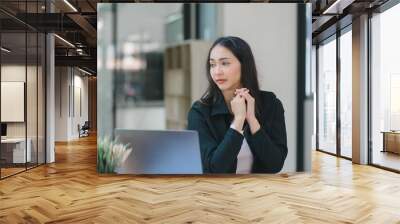 The stressed and exhausted millennial Asian businesswoman is tired after using a laptop while working remotely on a computer at a modern office. Wall mural