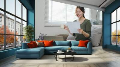 young asian businesswoman working from home on a laptop while drinking coffee and reading paperwork  Wall mural