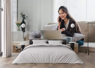 Young asian businesswoman working from home with laptop and cell phone. Work life balance concept Wall mural