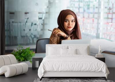 Young asian muslim business woman in smart casual wear discussing business and smiling while sitting in the creative coworking. Wall mural