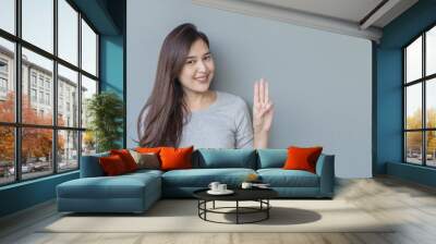 Closeup asian woman holds up three fingers with smile face on blurred cement wall textured background with copy space Wall mural