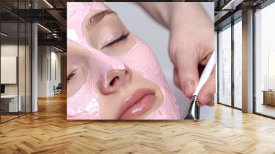 Photo of a woman getting a facial treatment with a pink mask in a beauty salon on a white background Wall mural