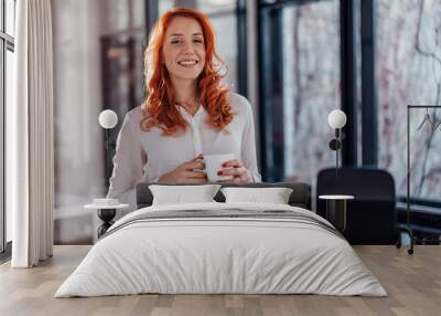 Portrait of a young business woman drinking coffee at the desk in the office. Wall mural