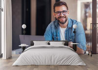 Portrait of attractive smiling man sitting in office and looking at camera. Wall mural