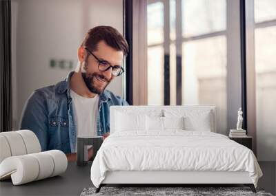 Smiling young businessman working online with digital tablet while standing by window. Wall mural