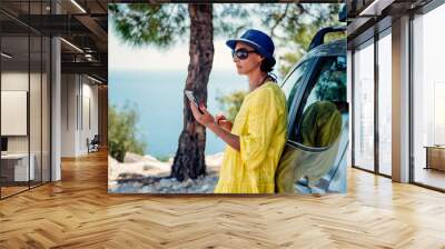 Woman standing by the car and using smart phone Wall mural